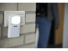 Charger l'image dans la galerie, Veilleuse blanche branchée sur une prise murale. Une personne est en arrière-plan, légèrement floue.