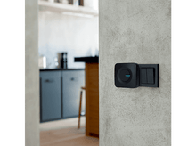 Charger l'image dans la galerie, Interrupteur de sonnette noir monté sur un mur gris. La cuisine est floue en arrière-plan.