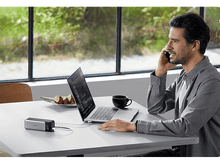 Charger l'image dans la galerie, Un homme au téléphone à une table avec un ordinateur portable et un chargeur.