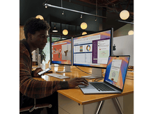 Charger l'image dans la galerie, Homme utilisant un ordinateur portable et un téléphone sur un bureau avec deux moniteurs.
