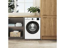 Charger l'image dans la galerie, Un lave-linge blanc avec une porte noire et un panneau de commande. À côté d'un meuble en bois.