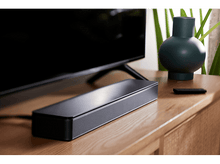 Charger l'image dans la galerie, Une barre de son noire est placée sur une table en bois devant un téléviseur noir et un vase.