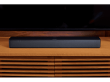 Charger l'image dans la galerie, Barre de son Bose sur un meuble en bois avec une télévision en arrière-plan.