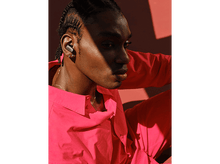 Charger l'image dans la galerie, Un homme à la peau foncée portant une chemise rouge et des écouteurs gris. Il regarde ailleurs.