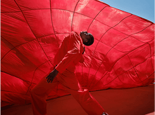 Charger l'image dans la galerie, Personne en combinaison rouge posant devant un grand tissu rouge.