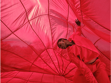 Charger l'image dans la galerie, Personne en vêtements rouges à l'intérieur d'un grand parachute rouge. Tissu cousu.