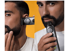 Charger l'image dans la galerie, Un homme se rase la barbe avec une tondeuse noire. Le fond est orange.