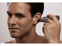 Charger l'image dans la galerie, Un homme se coupe les poils d'oreille avec un petit rasoir électrique. Il se regarde.