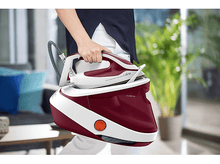 Charger l'image dans la galerie, Une personne tenant un fer à repasser rouge et blanc, avec un générateur de vapeur en arrière-plan.