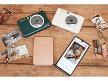 Charger l'image dans la galerie, Quatre appareils photo et un smartphone sur une table en bois, avec des photos éparpillées autour des appareils.