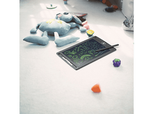 Charger l'image dans la galerie, Une tablette de dessin avec des dessins verts et bleus. Une peluche, une voiture jouet et des fruits en plastique au sol.