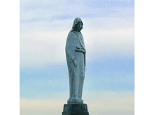 Charger l'image dans la galerie, Statue d'une femme vêtue d'une robe sur un piédestal, sous un ciel bleu et nuageux.
