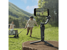 Charger l'image dans la galerie, Un cardan sur un trépied enregistre un homme, une fille et une charrette courant dans un champ herbeux.