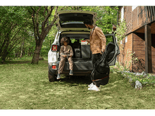 Charger l'image dans la galerie, Famille rangeant de l'équipement dans le coffre d'une voiture ; une personne tient un étui de guitare.
