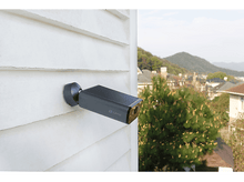 Charger l'image dans la galerie, Une caméra de sécurité sur un mur blanc. Elle est gris foncé avec une lentille dorée.