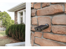Charger l'image dans la galerie, Caméra de sécurité noire montée sur un mur de briques à côté d'une maison.