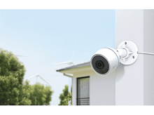 Charger l'image dans la galerie, Caméra de sécurité blanche montée sur un mur, donnant sur une cour verte.