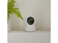 Charger l'image dans la galerie, Caméra de sécurité blanche sur une étagère avec une plante. La marque est EZVIZ.
