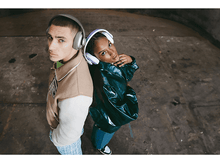 Charger l'image dans la galerie, Deux personnes portant des écouteurs, dos à dos, dans un environnement en béton.