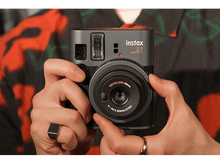 Charger l'image dans la galerie, Une personne tient un appareil photo gris Instax Mini 41. L'arrière-plan est une personne en chemise à motifs.