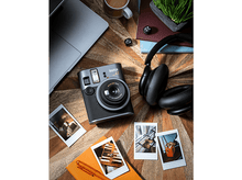 Charger l'image dans la galerie, Un appareil photo Instax Mini 41 est posé sur une table en bois avec un casque, un ordinateur portable et des photos.