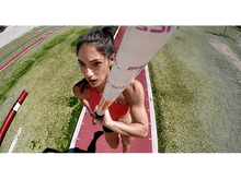 Charger l'image dans la galerie, Sauteuse à la perche féminine en plein saut, tenant une perche, regardant en haut, sur une piste.