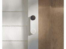 Charger l'image dans la galerie, Une sonnette blanche sur un mur blanc. Il y a une porte en bois en arrière-plan. C'est une journée ensoleillée.