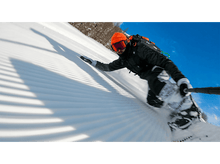 Charger l'image dans la galerie, Un snowboardeur dévalant une pente enneigée par une journée ensoleillée. Le ciel est bleu.