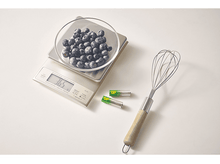 Charger l'image dans la galerie, Une balance de cuisine numérique avec des myrtilles dans un bol en verre, des piles et un fouet.