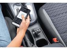 Charger l'image dans la galerie, La main d'une personne tenant un téléphone dans une voiture, à côté d'un chargeur de voiture.