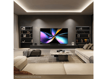 Charger l'image dans la galerie, Salon avec grande TV au mur, canapé, table basse. Étagères et murs sombres.