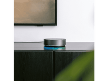 Charger l'image dans la galerie, Hub domotique sur un meuble noir avec une télévision en arrière-plan.