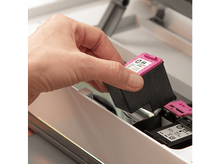 Charger l'image dans la galerie, Une main insère une cartouche d'encre HP noire et rose dans une imprimante blanche.