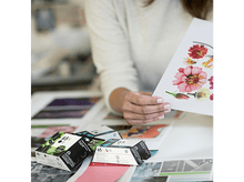 Charger l'image dans la galerie, Femme tenant une feuille avec des imprimés floraux, avec des cartouches d'encre devant elle.