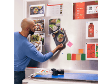 Charger l'image dans la galerie, Un homme regarde des images sur un tableau argenté avec des échantillons de couleurs et un appareil photo.