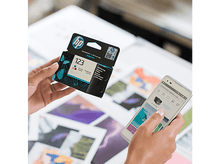 Charger l'image dans la galerie, Mains tenant une boîte de cartouches d'encre et un smartphone, montrant l'interface de l'application d'impression.