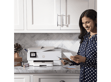 Charger l'image dans la galerie, Femme tenant des papiers près d'une imprimante, debout dans la cuisine.