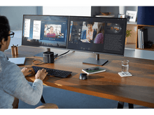 Charger l'image dans la galerie, Personne travaillant sur un bureau avec deux moniteurs affichant un appel vidéo et des données.