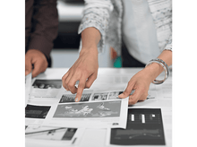 Charger l'image dans la galerie, Deux personnes pointant des papiers sur une table. Les papiers ont des graphiques et une carte. L'accent est mis sur une main pointant vers un graphique.