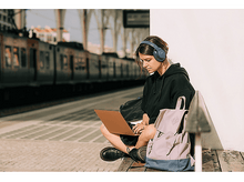 Charger l'image dans la galerie, Femme avec casque et ordinateur portable assise sur un banc, train en arrière-plan.