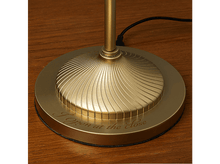 Charger l'image dans la galerie, Base de lampe dorée avec texte gravé, sur surface en bois.