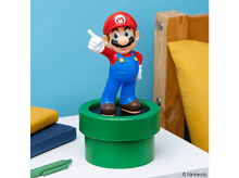 Charger l'image dans la galerie, Figurine de Mario debout sur un tuyau vert, pointant, sur une table blanche, avec fond bleu et jaune.