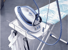 Charger l'image dans la galerie, Un fer à repasser blanc et bleu sur un support avec des cintres et des chemises. Une table à repasser avec un motif floral bleu.