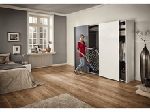 Charger l'image dans la galerie, Femme en chemise rouge tient un étendoir, debout dans une chambre avec une grande armoire.