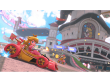 Charger l'image dans la galerie, Princesse Peach conduisant un kart rouge sur une piste. Bâtiments et autres coureurs en arrière-plan.
