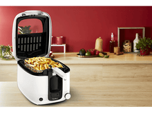 Charger l'image dans la galerie, Une friteuse blanche avec des frites à l'intérieur, sur un comptoir en bois, avec un mur rouge en arrière-plan.