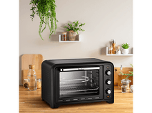 Charger l'image dans la galerie, Four de comptoir noir avec porte vitrée, sur une surface en bois, plantes au-dessus.