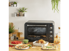 Charger l'image dans la galerie, Un four noir avec de la nourriture sur le comptoir. Comprend un poulet entier, une pizza et des légumes. Plantes en arrière-plan.