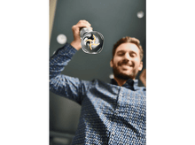 Charger l'image dans la galerie, Un homme tenant un mixeur plongeant argenté, lames visibles, incliné vers le haut avec un visage souriant.