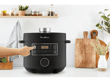 Charger l'image dans la galerie, Une autocuiseur Moulinex noir sur un comptoir blanc avec une main appuyant sur un bouton.